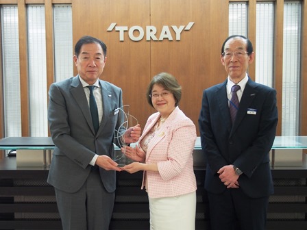 Toray’s Executive Vice President Abe (left) and Senior Director for Intellectual Property Eiichi Wada (right) receive the trophy from Ms. Tanahashi